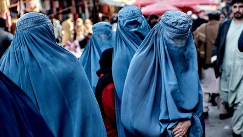 Die vier Frauen sind komplett mit blauen Tüchern verhüllt. Dahinter Marktbesucher.