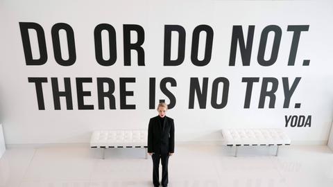 Im Still aus "The Dropout" steht Amanda Seyfried in schwarzen Klamotten vor einer Wand mit dem Yoda-Zitat: "Do or do not. There is no try." 