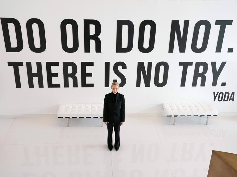 Im Still aus "The Dropout" steht Amanda Seyfried in schwarzen Klamotten vor einer Wand mit dem Yoda-Zitat: "Do or do not. There is no try." 
