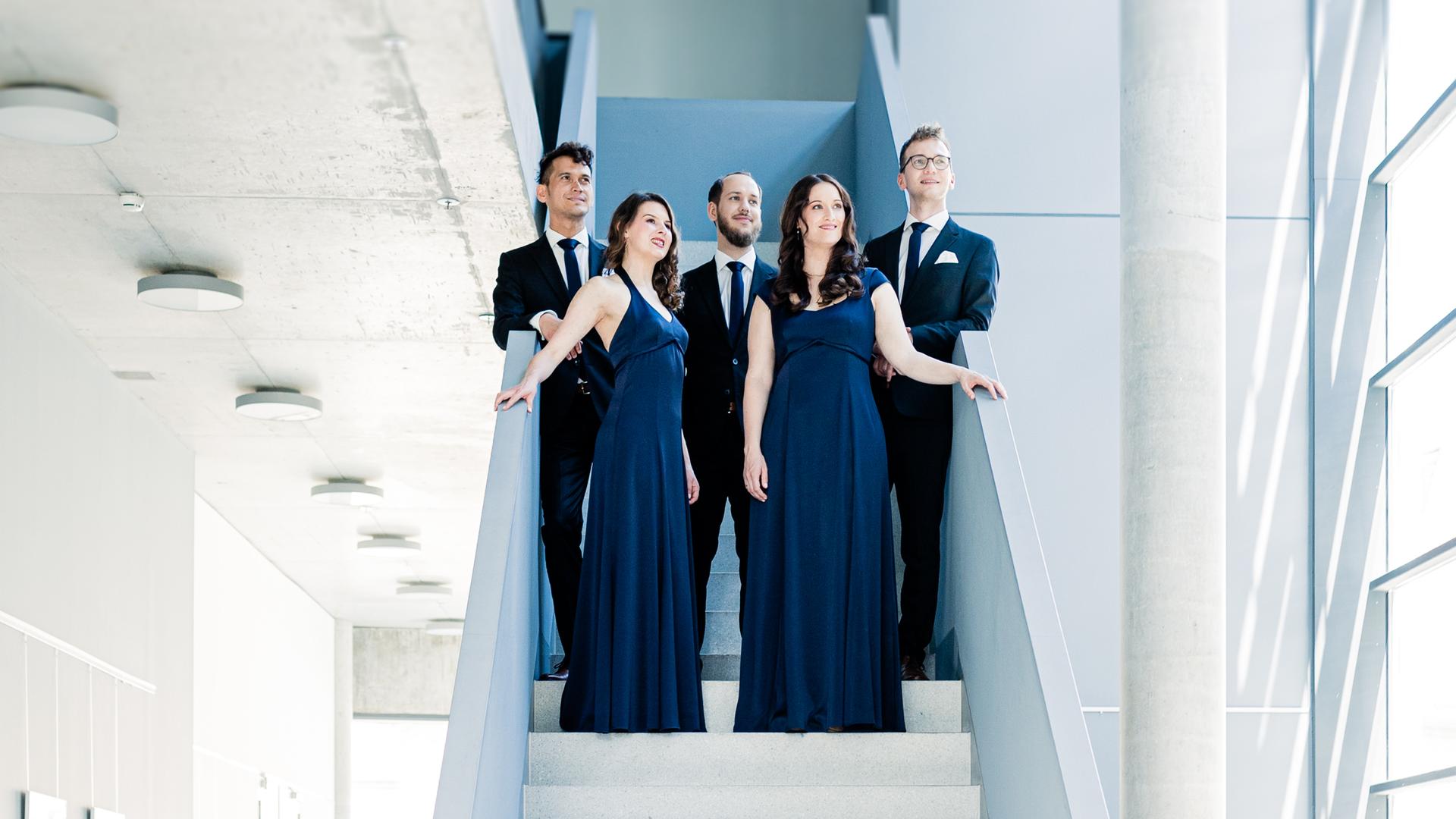Die fünf Musiker und Musikerinnen des Calmus Ensemble Leipzig stehen in Abendgarderobe auf einer weißen Treppe.