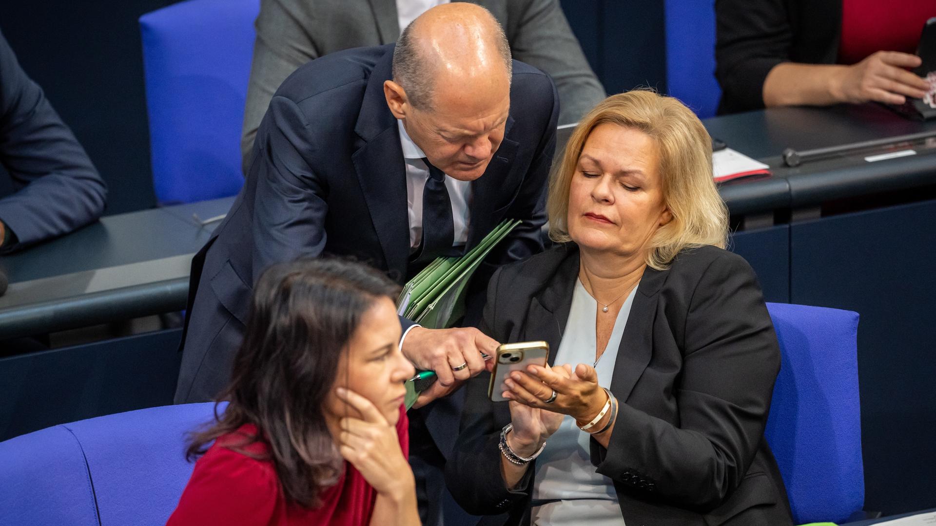 Bundesinnenministerin Nancy Faeser spricht mit Bundeskanzler Olaf Scholz im Deutschen Bundestag, daneben Bundesaußenministerin Annalena Baerbock.