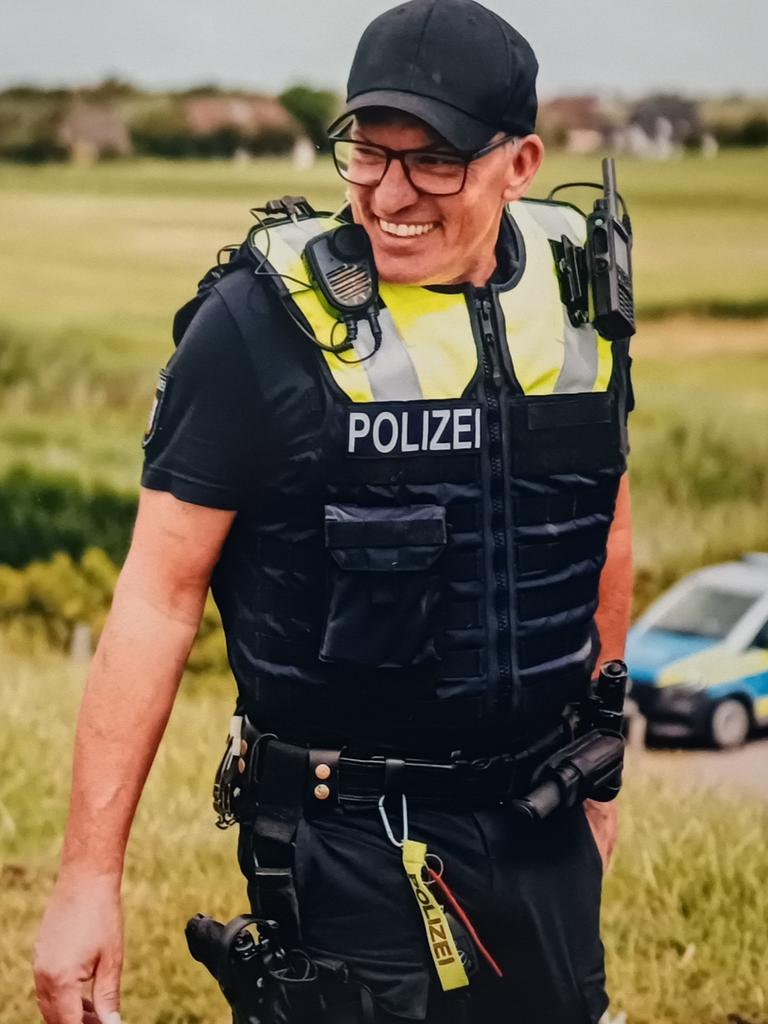 Der Inselpolizist Markus Stephan auf Pellworm, er ist in Uniform und lacht, im Hintergrund steht ein Polizeiauto.