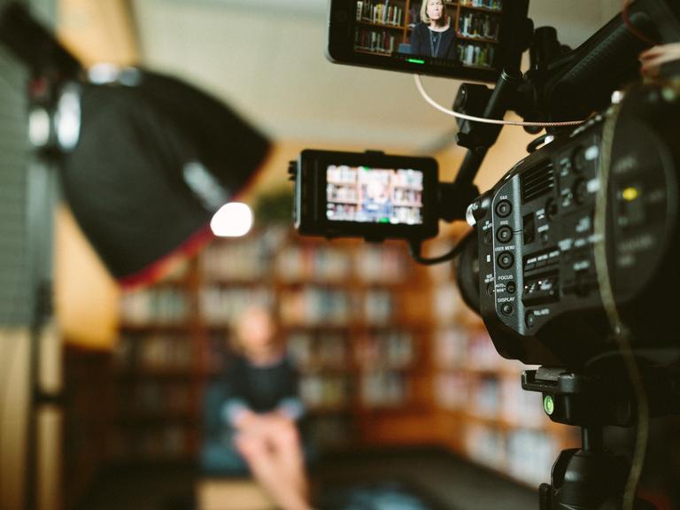 Großaufnahme einer Filmkamera, die ein im Unschärfebereich liegendes Set fotografiert