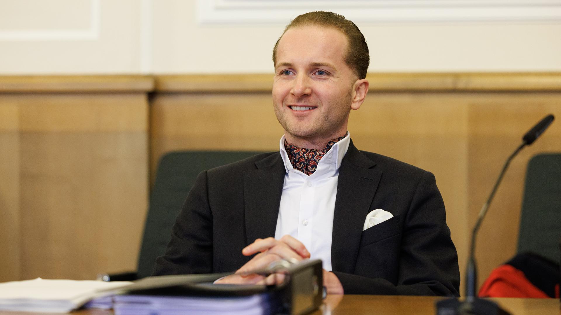 Der Angeklagte Hendrik Holt sitzt in einem Sitzungssaal vom Landgericht und lacht.