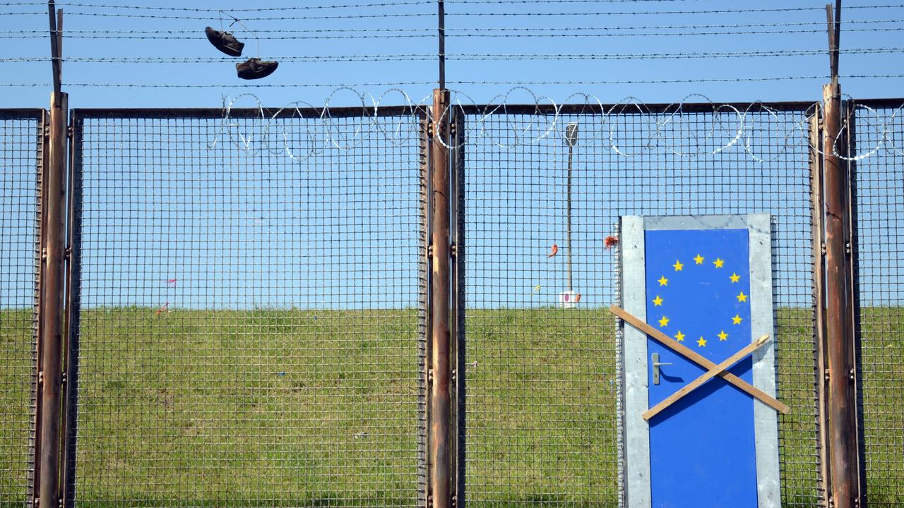 Symbolbild EU-Außengrenze: Zaun mit einer blauen EU-Tür, die mit zwei Holzbalken verbarrikadiert ist
