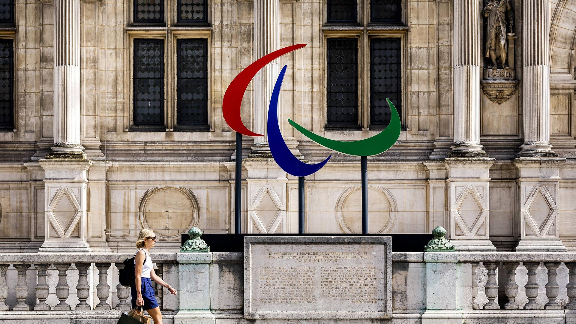 Das Logo der Paralympics vor einer Hauswand in Paris. Eine Frau läuft daran vorbei. Das Logo der Paralympics vor einer Hauswand in Paris. Eine Frau läuft daran vorbei.