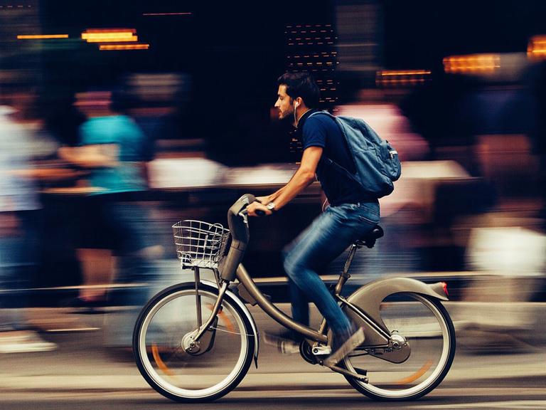 Ein junger Mann auf einem Fahrrad fährt schnell eine belebte Straße entlang. 