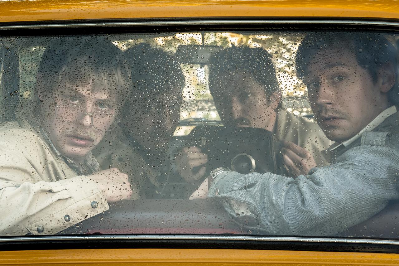 Im Still aus "Stasikomödie" schauen vier Männer mit belämmerten Gesichtsausdrücken aus der Heckscheibe eines Wagens. Einer von ihnen hat eine Kamera in der Hand.