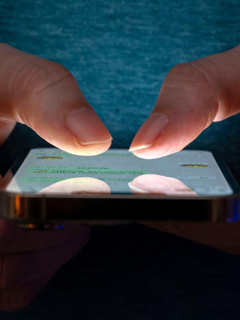 Eine Frau tippt auf einem Smartphone-Screen. Das Bild zeigt eine Person, die in einer schlecht beleuchteten Umgebung ein Smartphone benutzt. Die Beleuchtung hebt die Finger des Benutzers und den Bildschirm des Smartphones hervor.