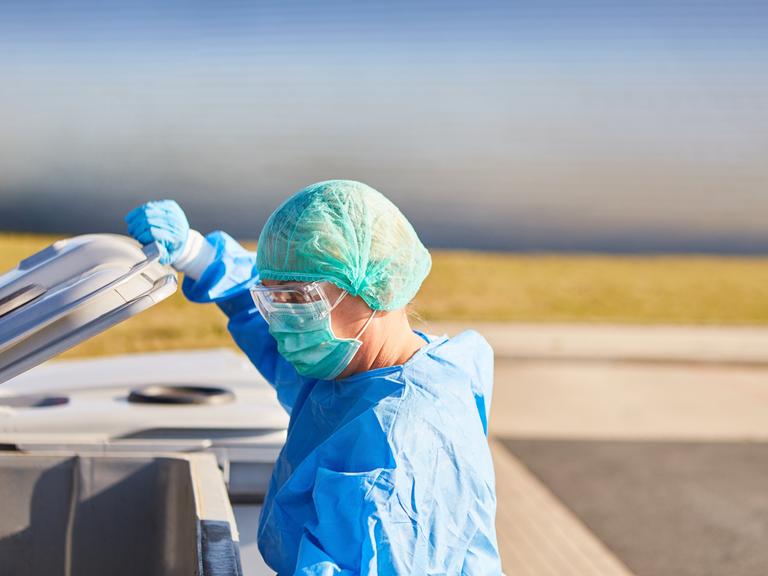 Die Putzkraft einer Klinik in Schutzkleidung öffnet eine Mülltonne.