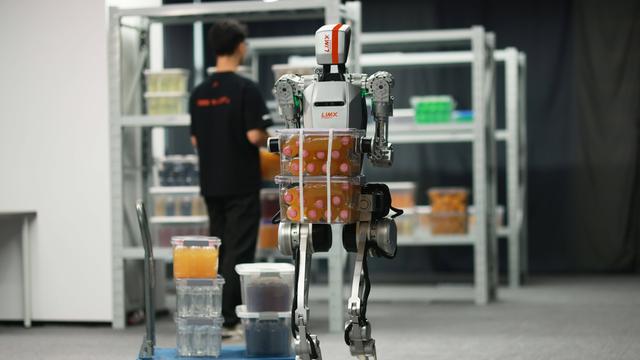 Ein humanoider Roboter trägt in einer Halle schwere Kisten