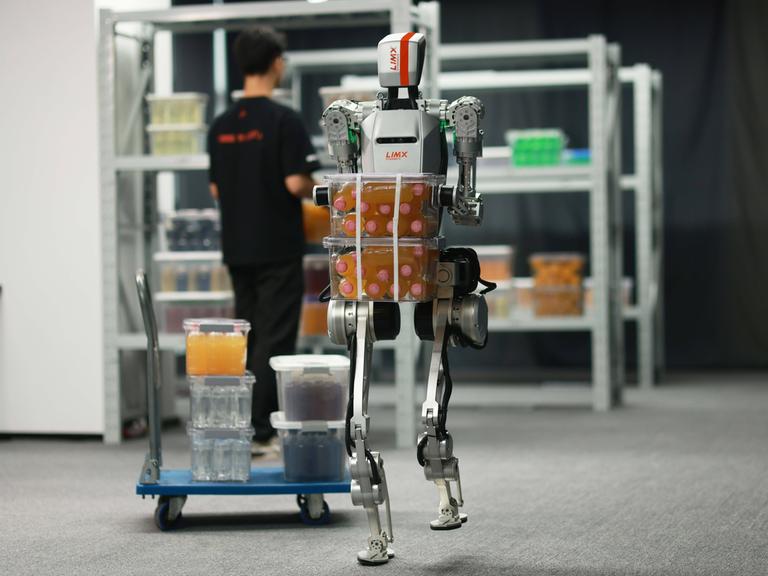 Ein humanoider Roboter trägt in einer Halle schwere Kisten