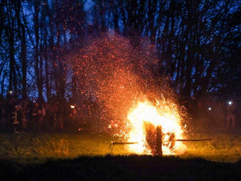 Ein hölzernes Osterrad, gefüllt mit Stroh, rollt beim Osterräderlauf brennend einen Hang hinunter.