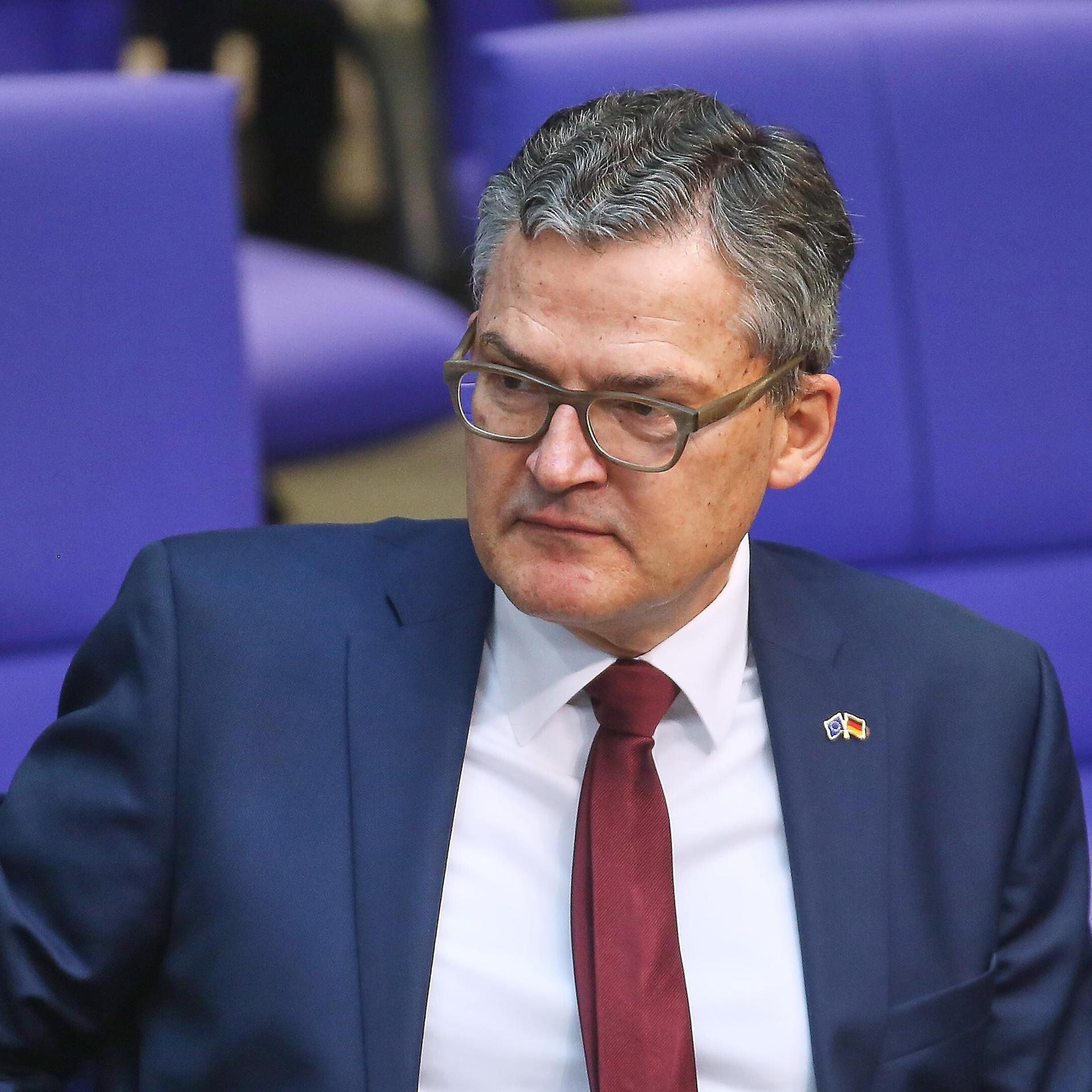 Der CDU-Abgeordnete Roderich Kiesewetter sitzt im Plenarsaal des Deutschen Bundestages. Er trägt eine Brille, einen blauen Anzug, weißes Hemd und rote Krawatte. 
