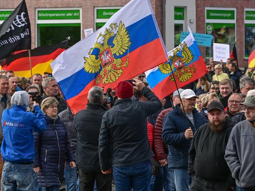 Viele Menschen nehmen an einer Protest-Demonstration teil und schwenken dabei unter anderem auch Russland-Fahnen und die deutsche Fahne. 