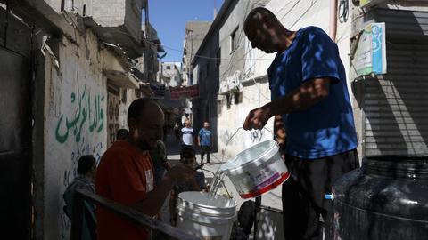Ein Mann in einem Flüchtlingscamp im südlichen Gazastreifen füllt einen Eimer mit Trinkwasser. Ein weiterer Mann hält den Eimer.