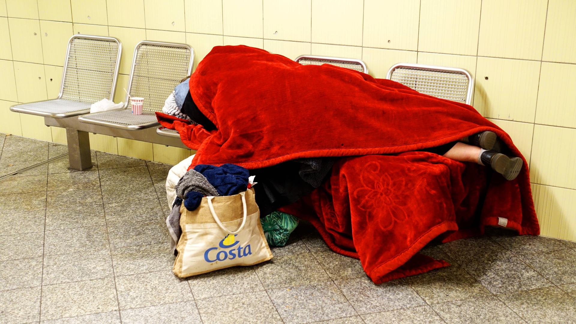 Obdachloser zugedeckt mit einer roten Decke schläft auf einer Bank in der U-Bahnstation Leopoldplatz. 