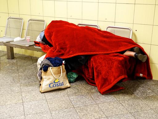 Obdachloser zugedeckt mit einer roten Decke schläft auf einer Bank in der U-Bahnstation Leopoldplatz. 