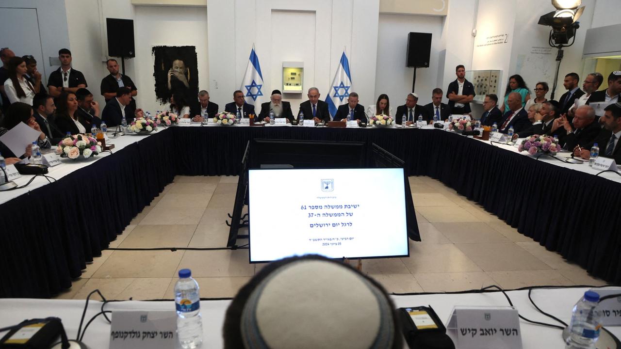 Blick auf die Regierungsmitglieder, die an vier im Quadrat angeordneten Tischen sitzen. Hinter dem Tisch mit Ministerpräsident Netanjahu (m.) stehen zwei israelische Flaggen.