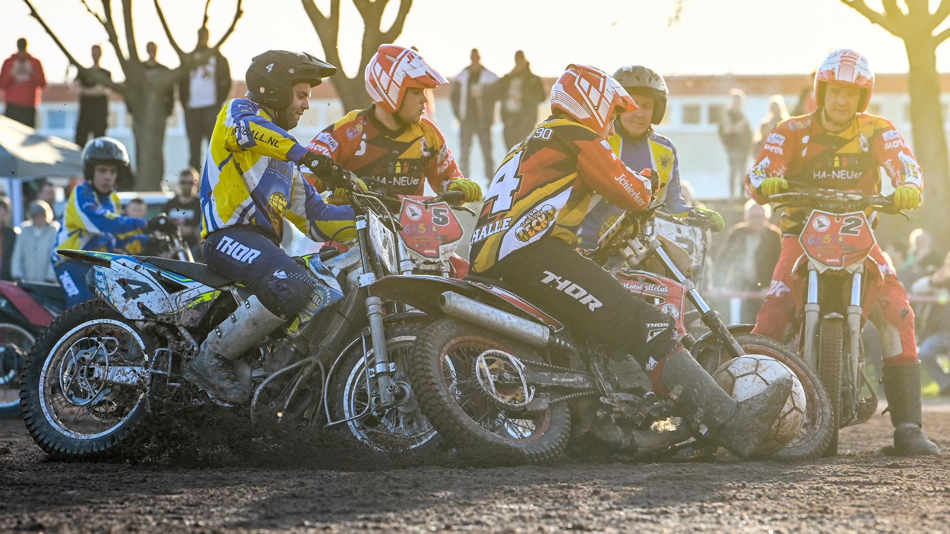 Mehrere Feldspieler auf Motorrädern wetteifern bei einer Motoball-Partie in Halle um den übergroßen Ball. Im Hintergrund sind Zuschauer zu sehen.