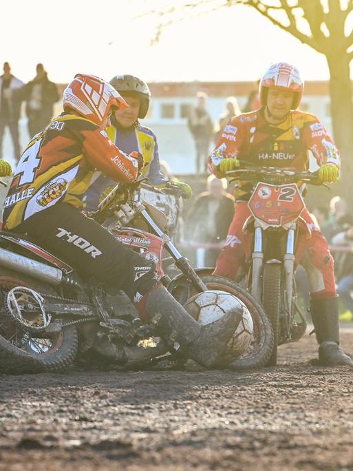 Mehrere Feldspieler auf Motorrädern wetteifern bei einer Motoball-Partie in Halle um den übergroßen Ball. Im Hintergrund sind Zuschauer zu sehen.