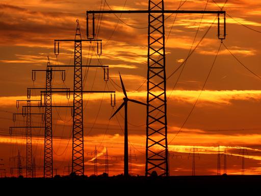 Ein Windrad steht im Abendlicht neben den Masten einer Stromtrasse. Ein Windrad steht im Abendlicht neben den Masten einer Stromtrasse.