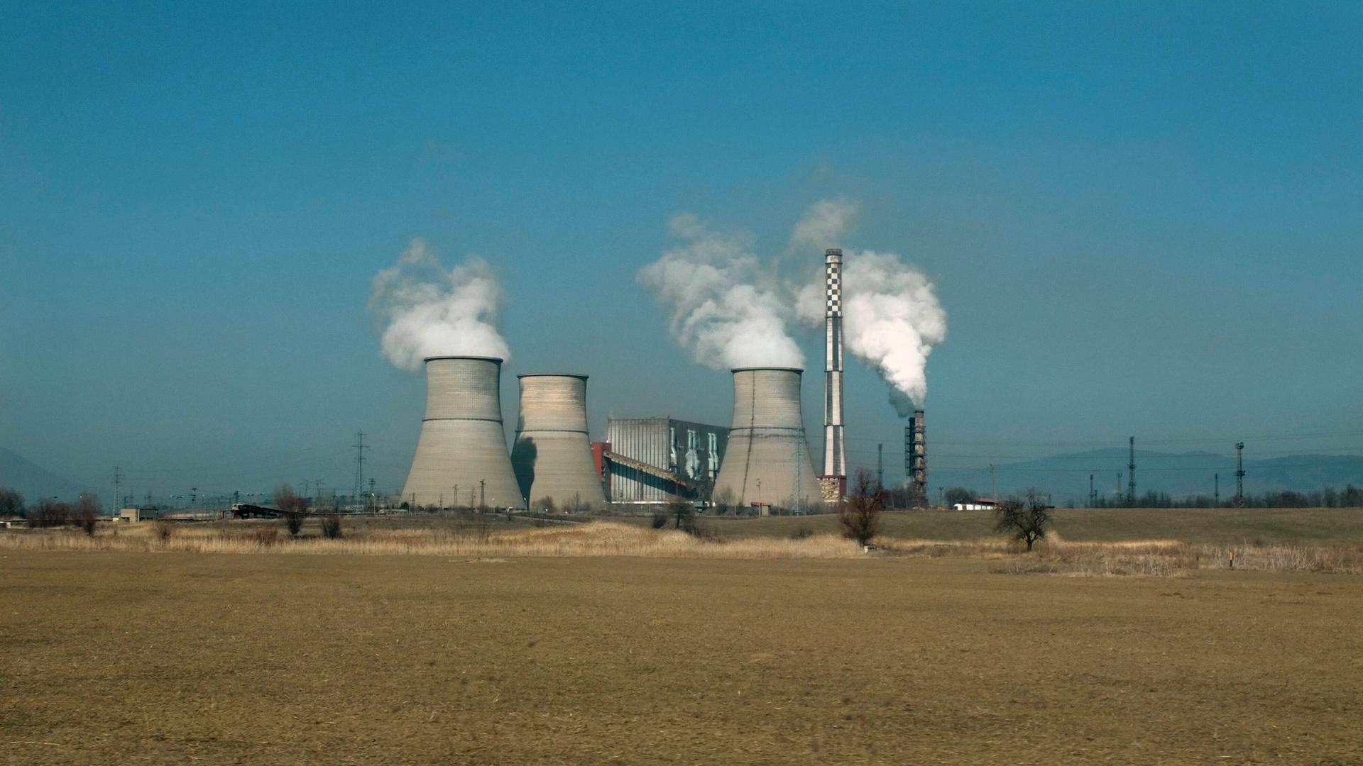 Das Kraftwerk Bobov Dol in Bulgarien steht dampfend vor blauem Himmel. Insgesammt sind drei Kühltürme zu sehen.