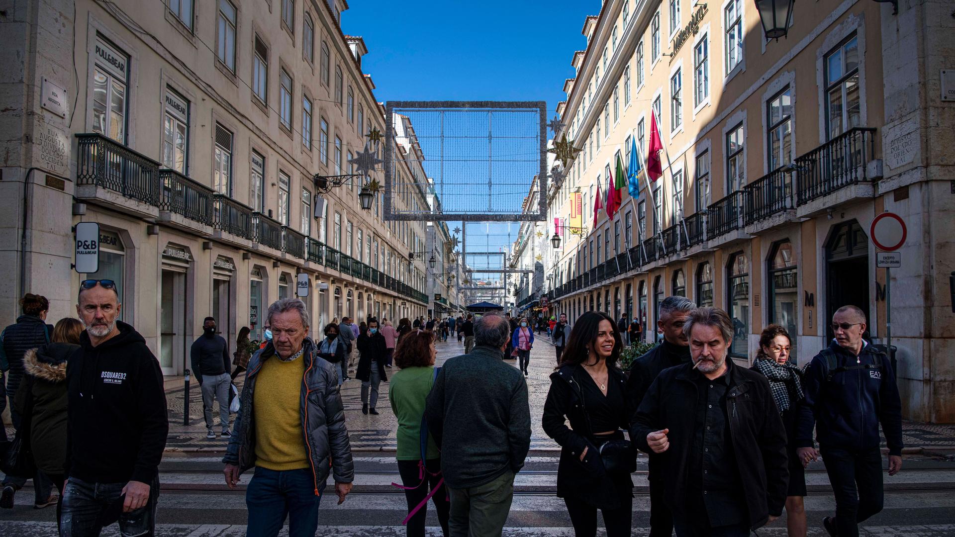 Auf einer Straße in Lissabon laufen Menschen. Rechts und links stehen schöne alte Häuser (26.11.2021)