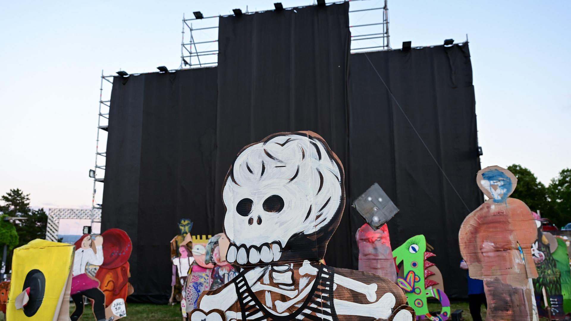 Von einem Metallgerüst hängen schwarze Stoffbahnen herunter. Auf der Wiese davor stehen Pappfiguren, die vorderste davon in Gestalt eines Skeletts mit Totenschädel. 