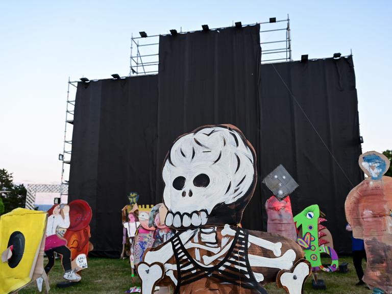 Von einem Metallgerüst hängen schwarze Stoffbahnen herunter. Auf der Wiese davor stehen Pappfiguren, die vorderste davon in Gestalt eines Skeletts mit Totenschädel. 