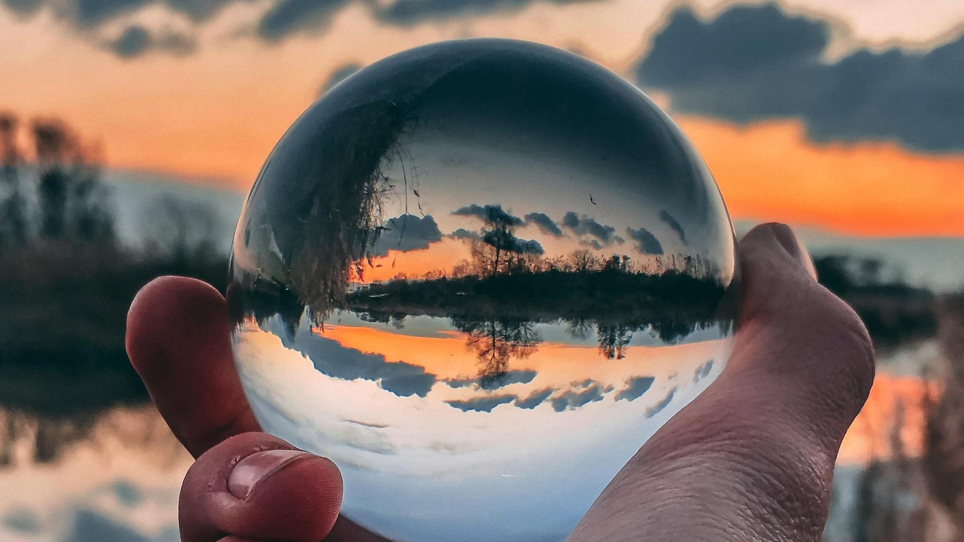 Ein Mann hält eine Glaskugel in der Hand, in der ein Sonnenuntergang mit umgekehrter Sicht der Landschaft erscheint.