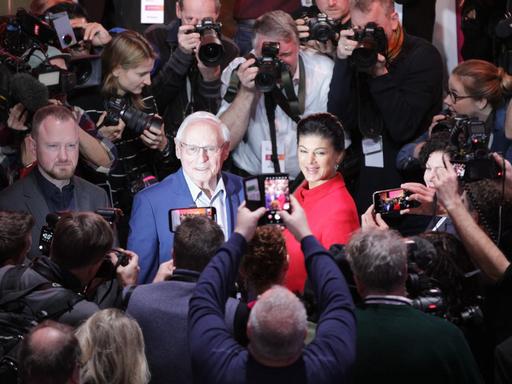  Die BSW-Politiker Oskar Lafontaine und Sahra Wagenknecht betreten den Saal und bekommen Applaus, um sie herum viele Fotografen und Kameraleute