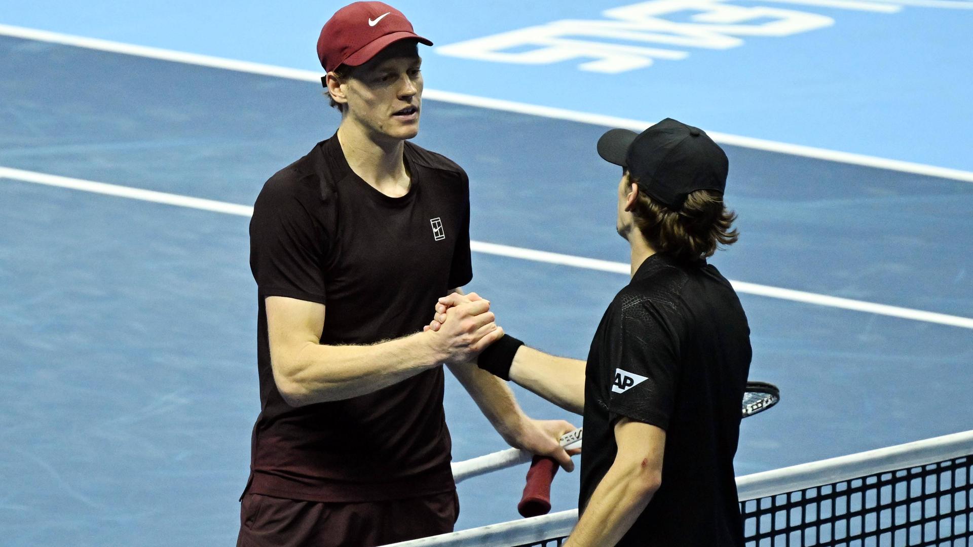 Jannik Sinner (l.) steht nach dem Sieg über Alex de Minaur im Endspiel. Beide Tennisspieler stehen am Netz und geben sich die Hand.