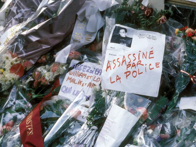 Blumen und beschriftete Zettel zum Gedenken an Malik Oussekine