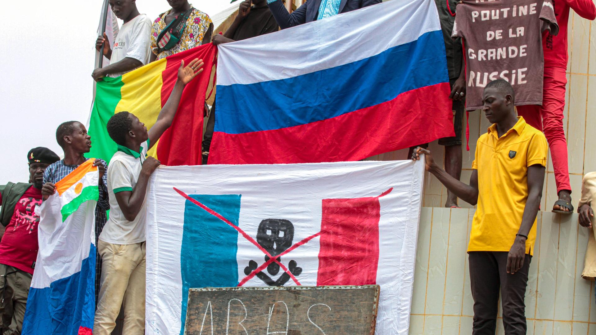 Nigerianische Demonstranten halten eine russische Flagge neben einer französischen Flagge, welche mit einem Totenkopf versehen ist.