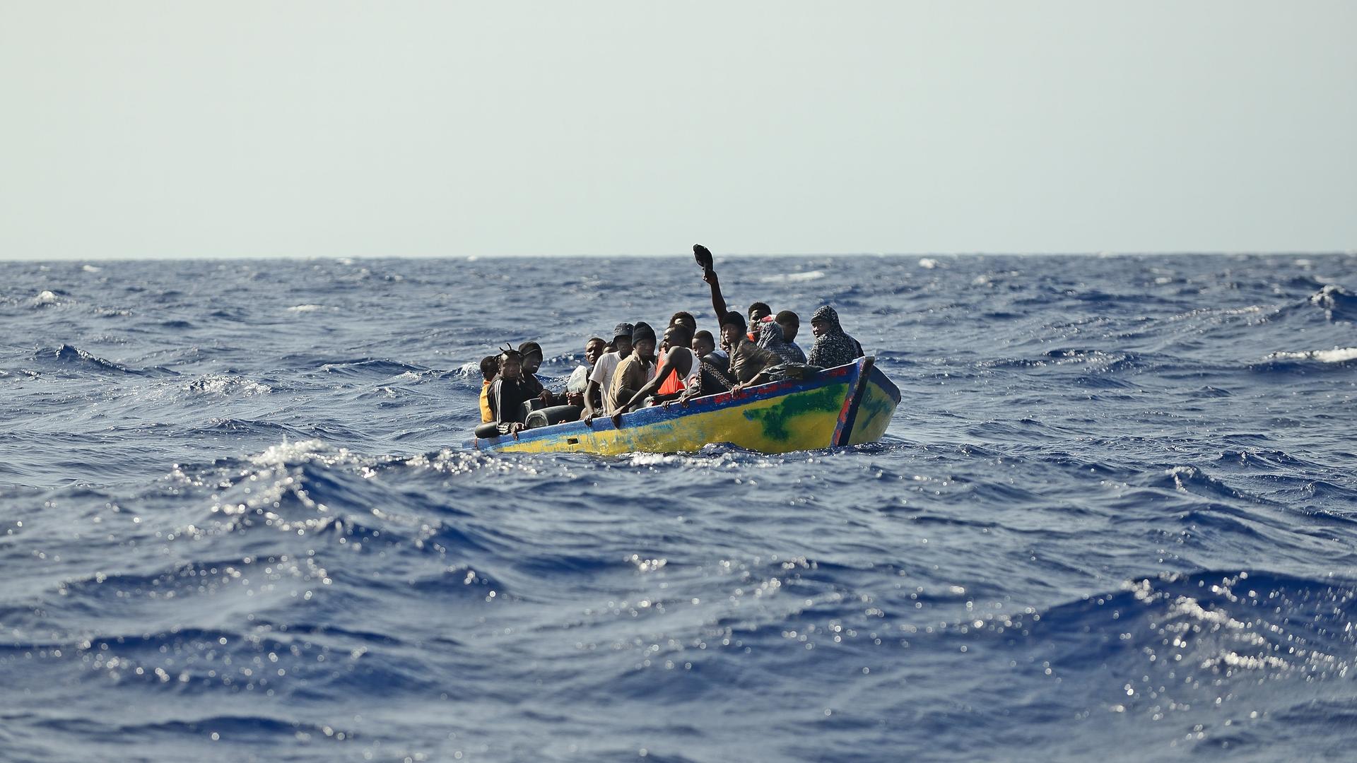 Flüchtling drängen sich in einem kleinen Holzboot auf offener See.