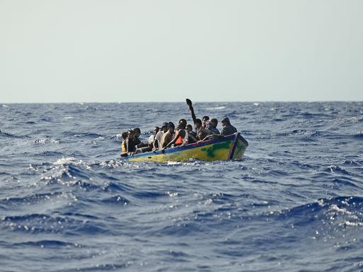 Flüchtling drängen sich in einem kleinen Holzboot auf offener See.