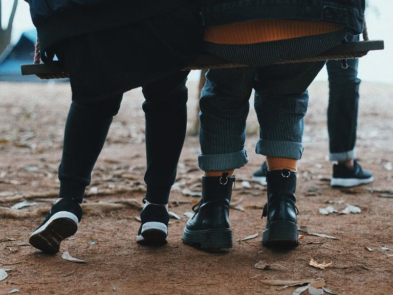 Zwei Kinder sitzen gemeinsam auf einer breiten Schaukel.