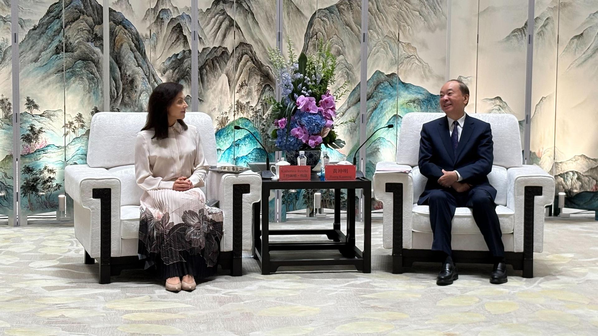 Bundeswirtschaftsministerin Katherina Reiche und der Parteisekretär der südchinesischen Provinz Guangdong, Huang Kunming, auf weißen Sesseln, zwischen ihnen ein kleiner Tisch mit Blumen