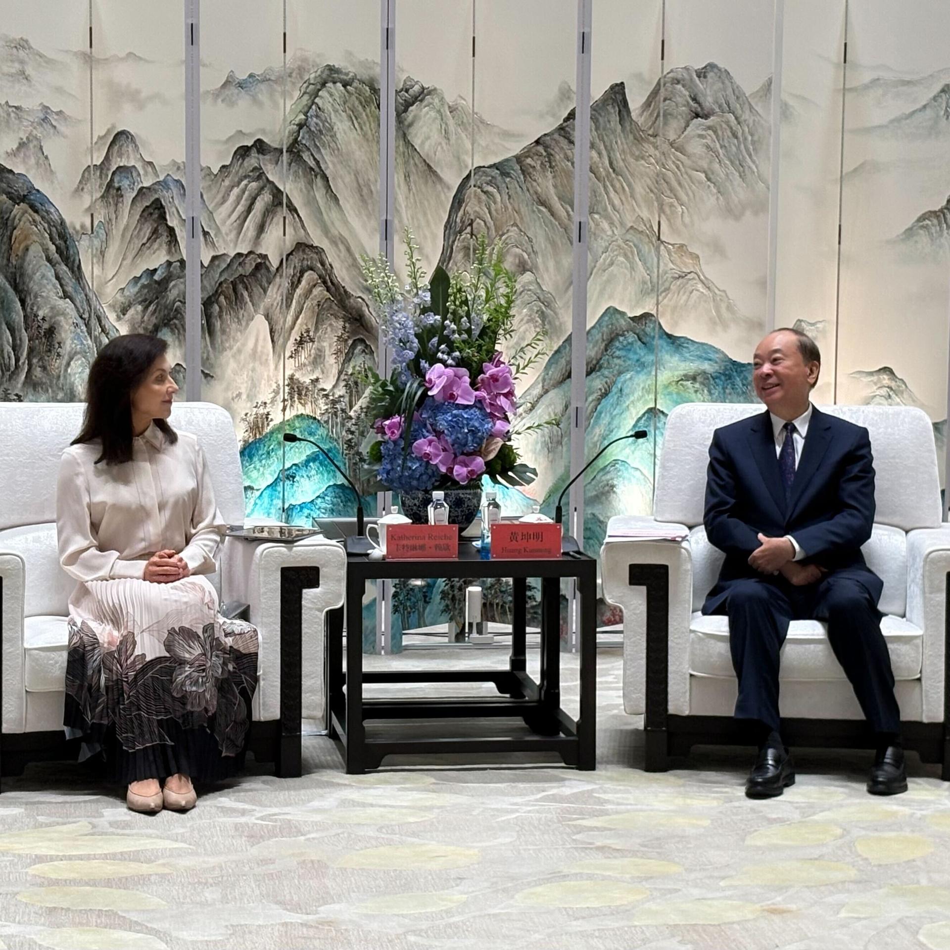 Bundeswirtschaftsministerin Katherina Reiche und der Parteisekretär der südchinesischen Provinz Guangdong, Huang Kunming, auf weißen Sesseln, zwischen ihnen ein kleiner Tisch mit Blumen