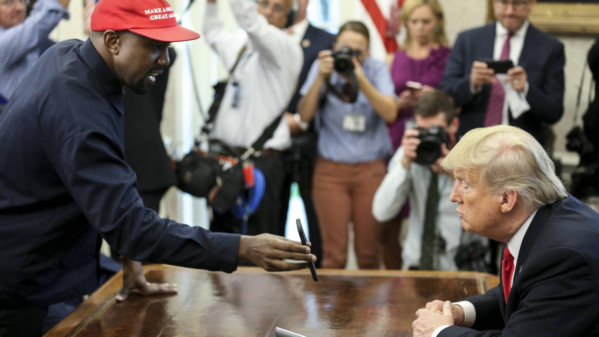 Kanye West zeigt Donald Trump sein Handy, umringt von Fotografen.