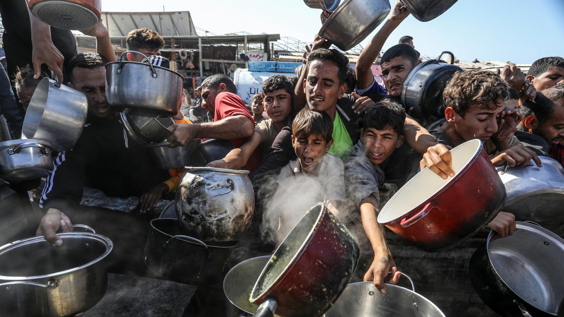 Viele junge Männer mit Töpfen versuchen an etwas Essbares zu kommen. Ihren Gesichtern sind Hunger und Not anzusehen.