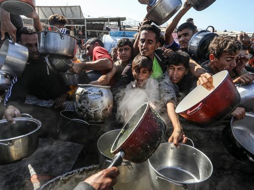 Viele junge Männer mit Töpfen versuchen an etwas Essbares zu kommen. Ihren Gesichtern sind Hunger und Not anzusehen.