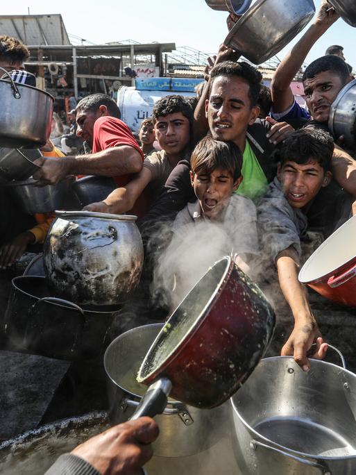 Viele junge Männer mit Töpfen versuchen an etwas Essbares zu kommen. Ihren Gesichtern sind Hunger und Not anzusehen.