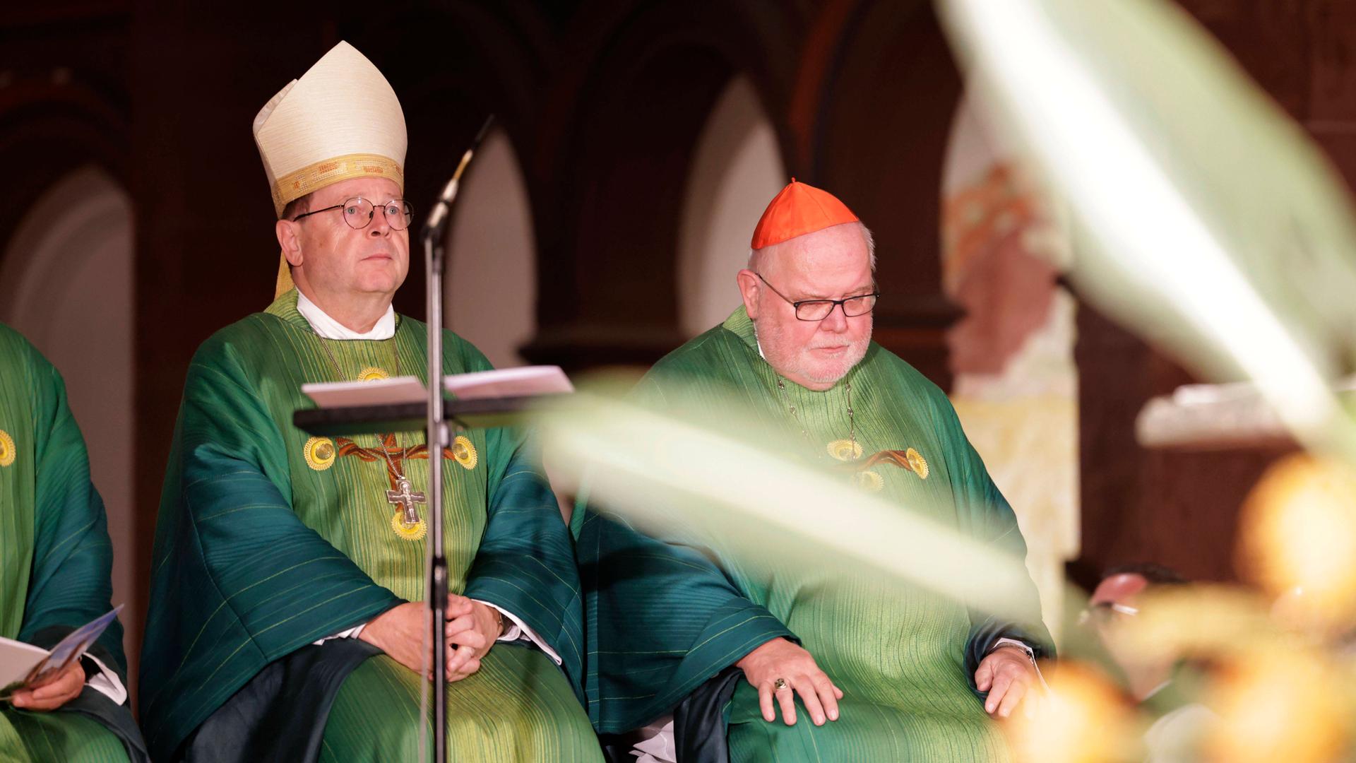 Zwei Männer, Georg Bätzing (links), und Reinhard Marx, sitzen in einenm grünen Gewand in der Kirche St. Bonifatius in Wiesbaden.  