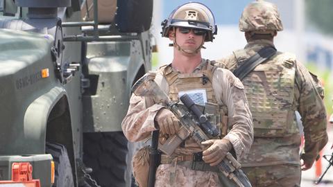 Das Bild zeigt zwei schwer bewaffnete US-Soldaten in Kampfmontur neben einem Militärfahrzeug.