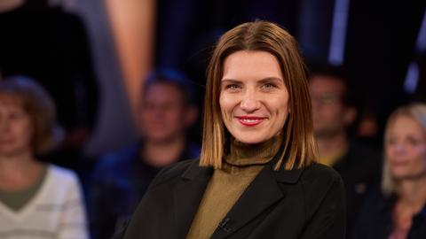 Magdalena Gössling, Autorin und ehemalige Ärztin, vor der Aufzeichnung der "NDR Talk Show" im Studio. Sie trägt einen braunen Rollkragenpullover und eine schwarze Jacke und lacht in die Kamera. Im Hintergrund ist das Publikum verschwommen auszumachen.