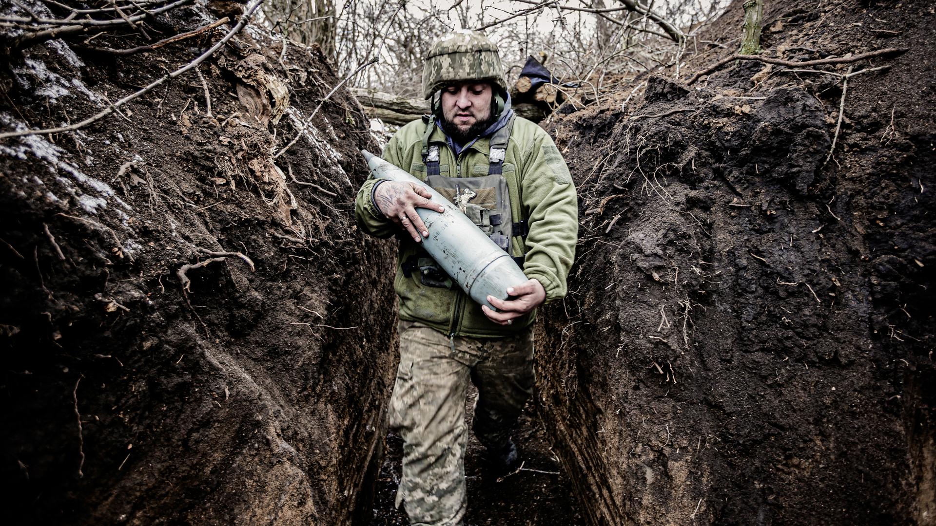 Ein Soldat an der Front in Donezk trägt schwere Munition durch einen Schützengraben.