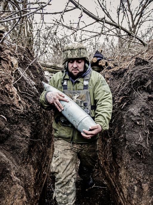 Ein Soldat an der Front in Donezk trägt schwere Munition durch einen Schützengraben.