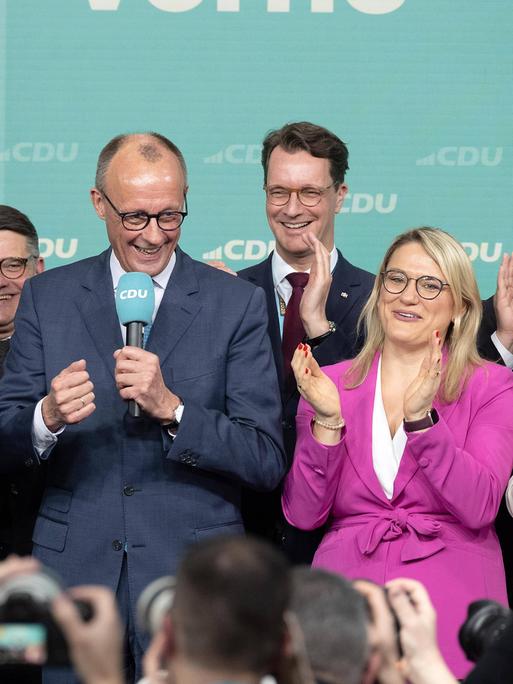 CDU-Vorsitzender Friedrich Merz steht am Abend der Bundestagswahl 2025 im Konrad-Adenauer-Haus in Berlin, umringt von weiteren Unionsmitgliederb und schaut dabei fröhlich.